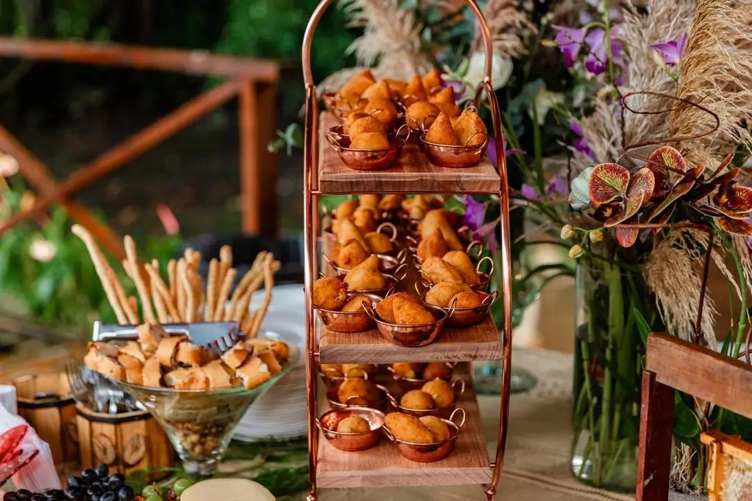 Prateleira de madeira com salgados e flores do buffet